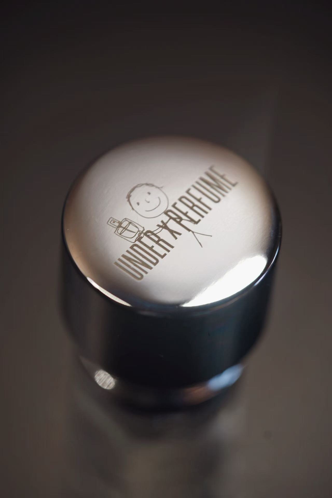 Close-up of perfume cap engraved with UNDER x PERFUME